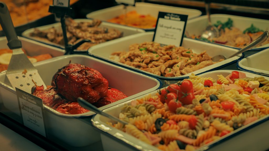 A diverse buffet selection featuring pasta salad, meats, and stuffed peppers.
